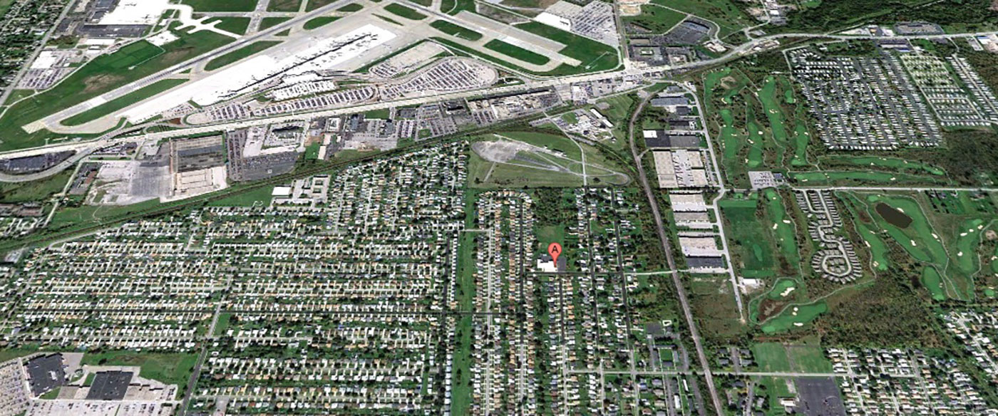 Aerial view of a suburban neighborhood with rows of houses, a large airport with runways and terminals at the top, and a golf course to the right; streets and green spaces are visible throughout.