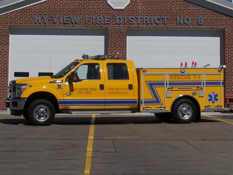 A yellow rescue fire truck labeled "Hy-View Fire Co. Inc. Rescue 7-1" is parked in front of a brick fire station with three white garage doors. The building's sign reads "HY-VIEW FIRE DISTRICT NO. 8.